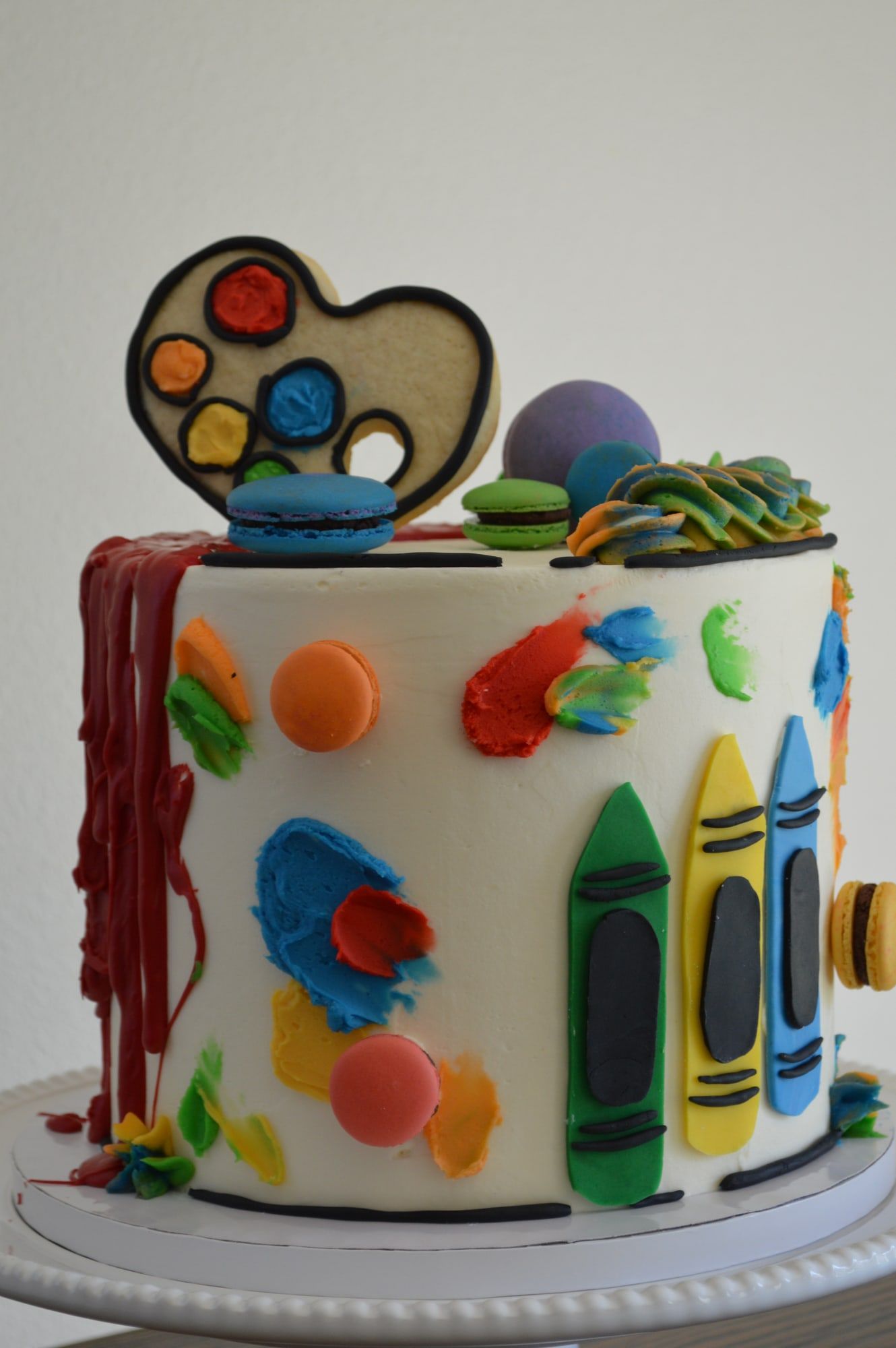 White cake decorated with buttercream paint splatters, fondant crayons and an artist palette