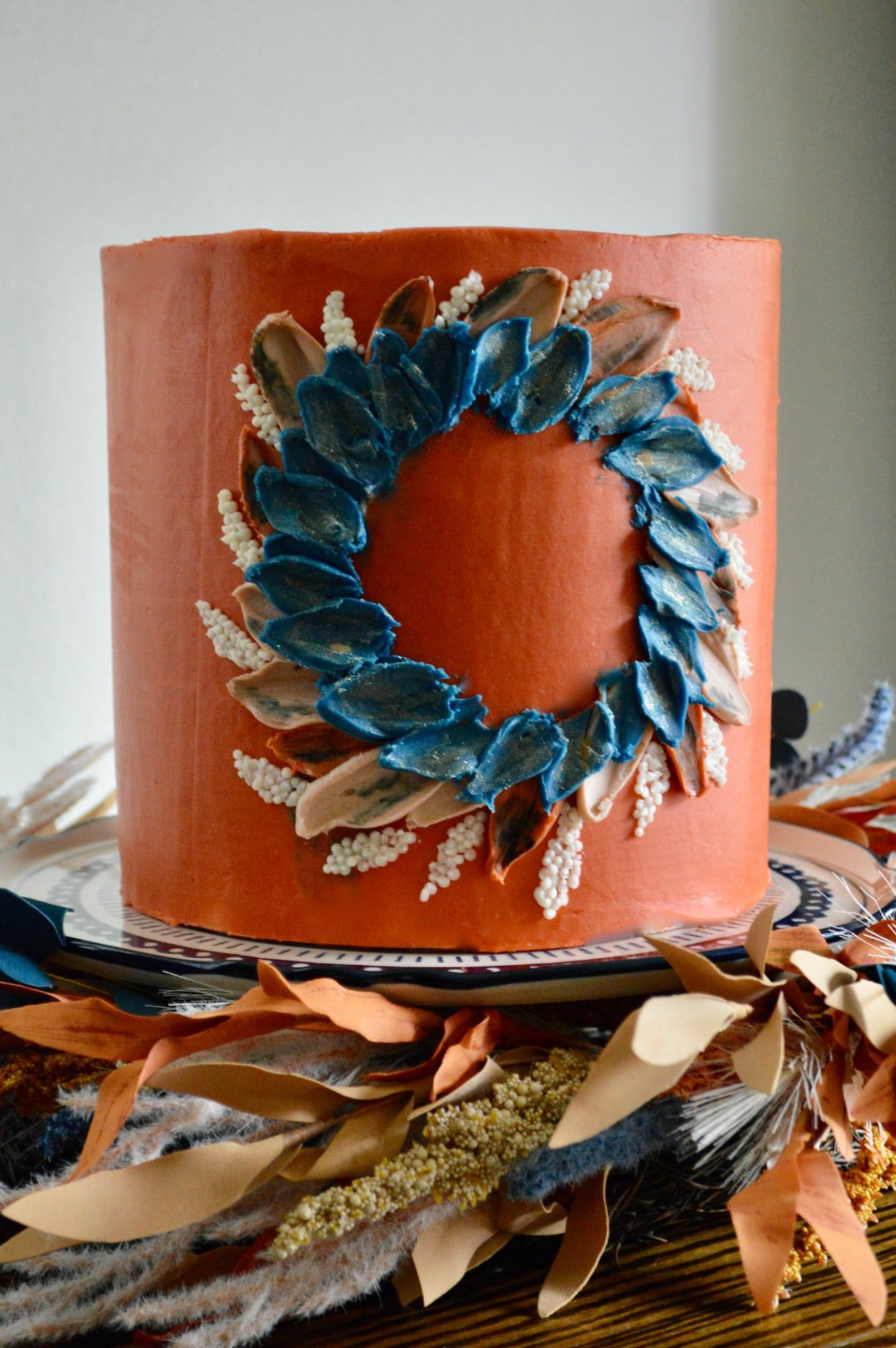 Terracotta buttercream cake ringed with a piped wreath of deep blue and cream leaves