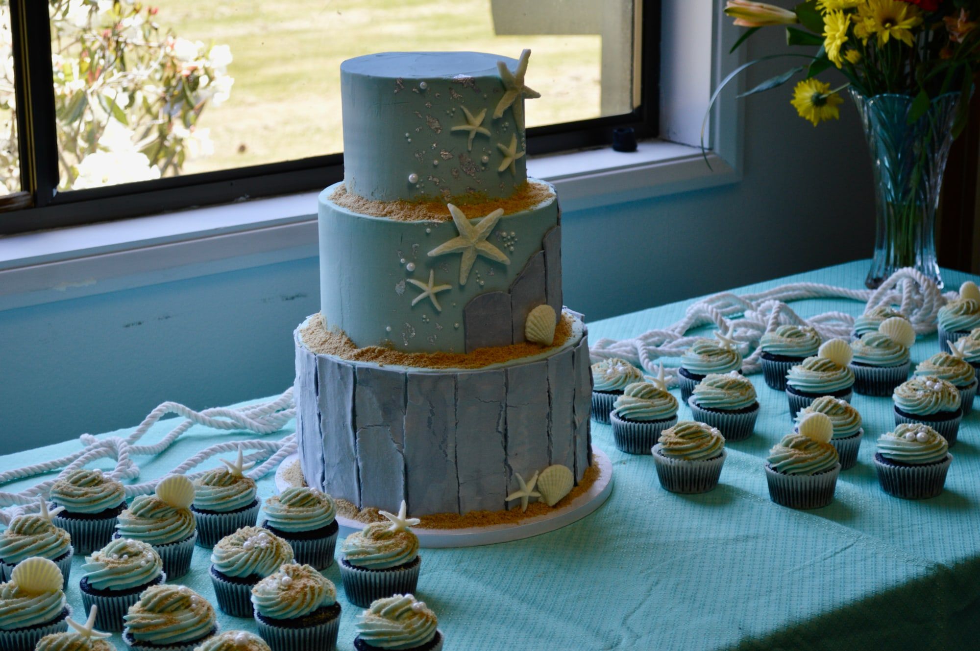Two-tier beach-themed cake with starfish and shells, set out with matching cupcakes