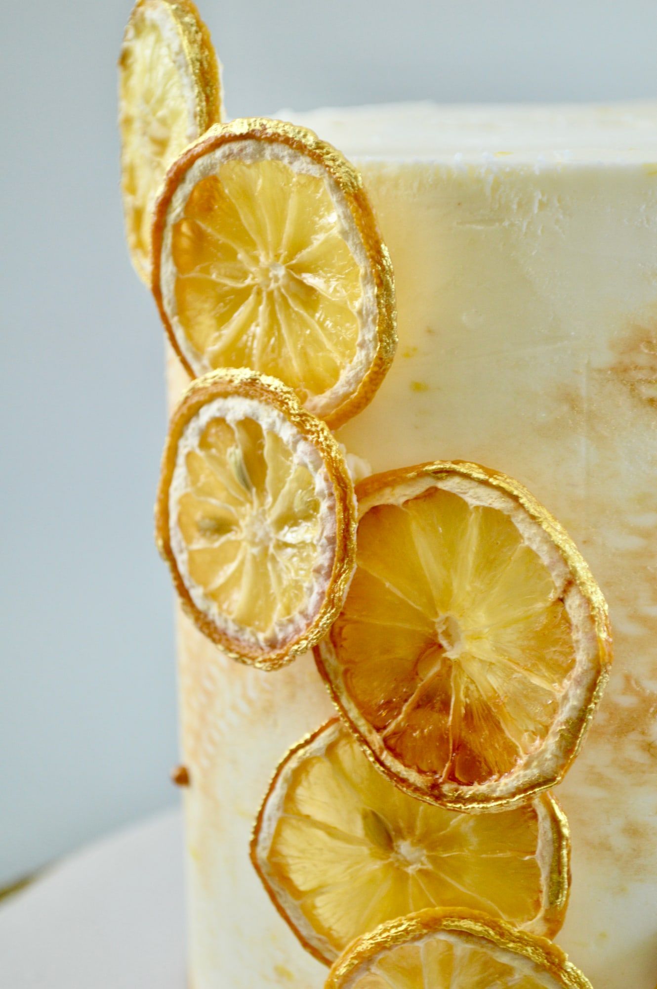 Close detail of candied lemon slices and gold leaf on textured white buttercream
