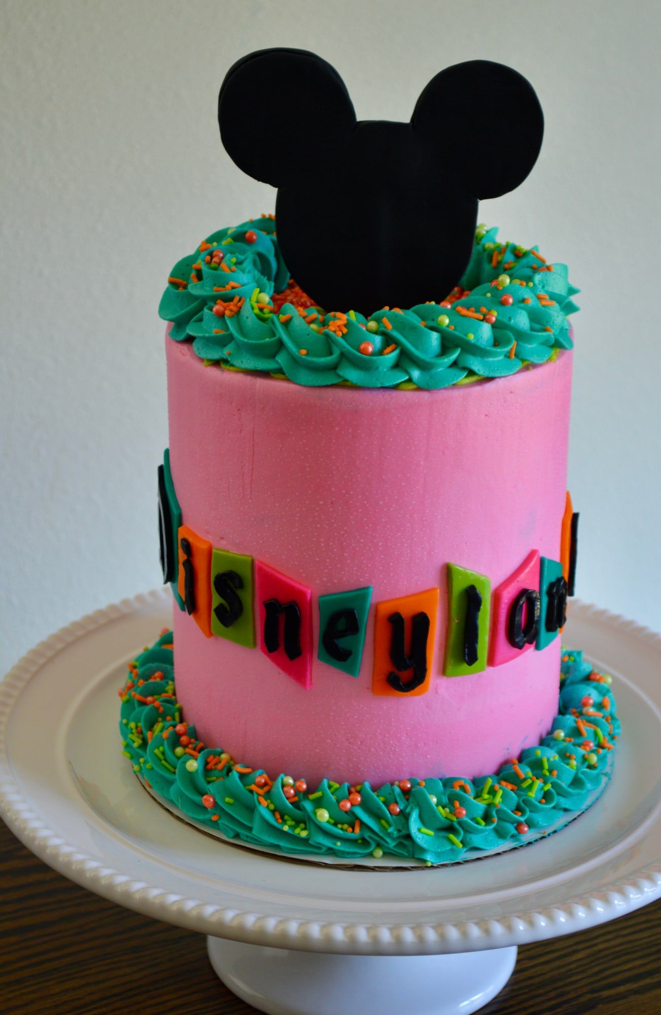 Pink and teal cake with a fondant graduation cap topper and piped green borders