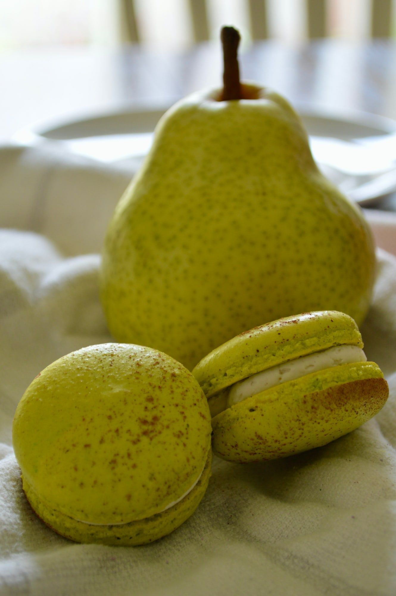 Pale green macarons resting beside a fresh pear