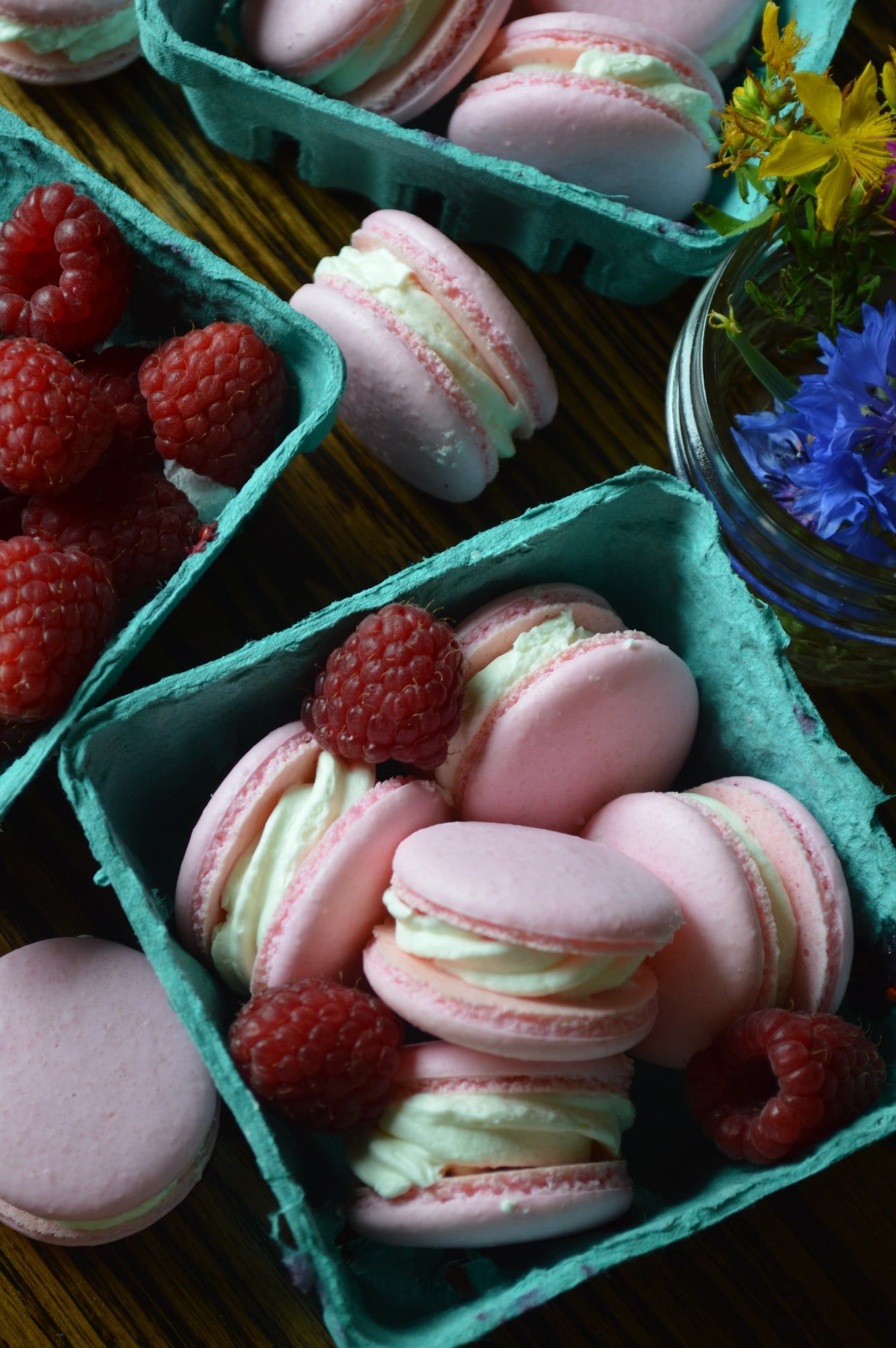 Pink and mint macarons in a berry carton with fresh raspberries