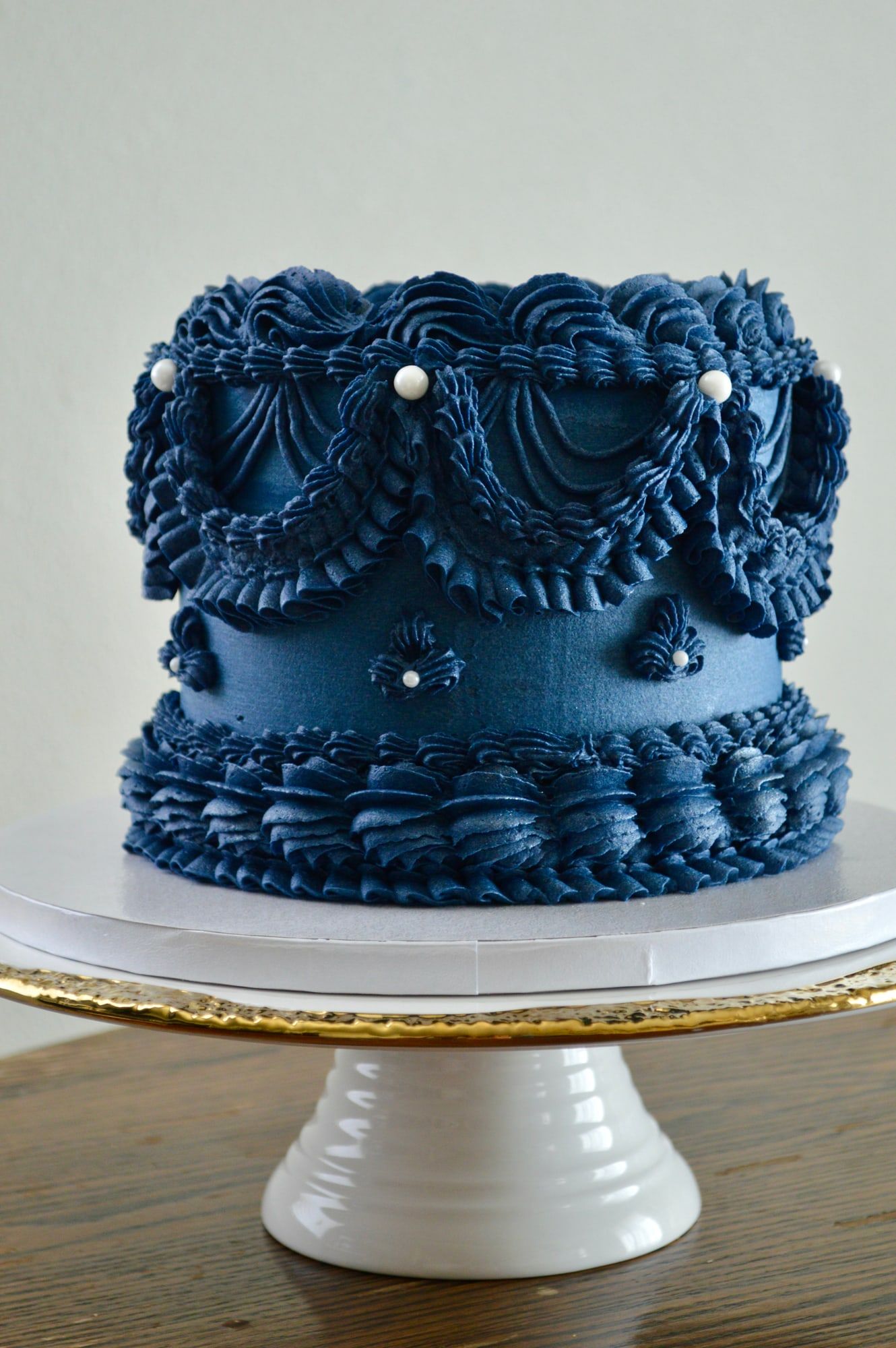 Navy blue cake covered in vintage-style piped ruffles, swags and pearls
