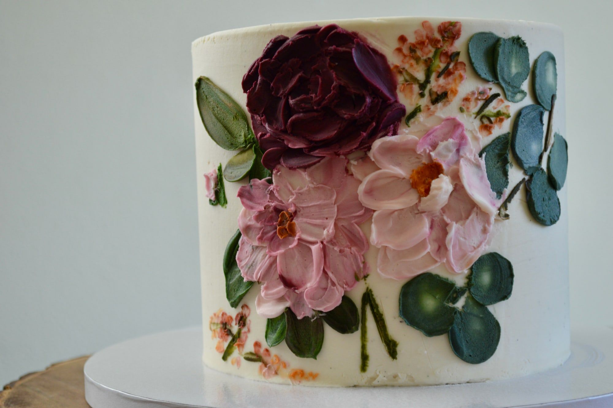Hand-painted buttercream flowers in burgundy and blush across a white cake