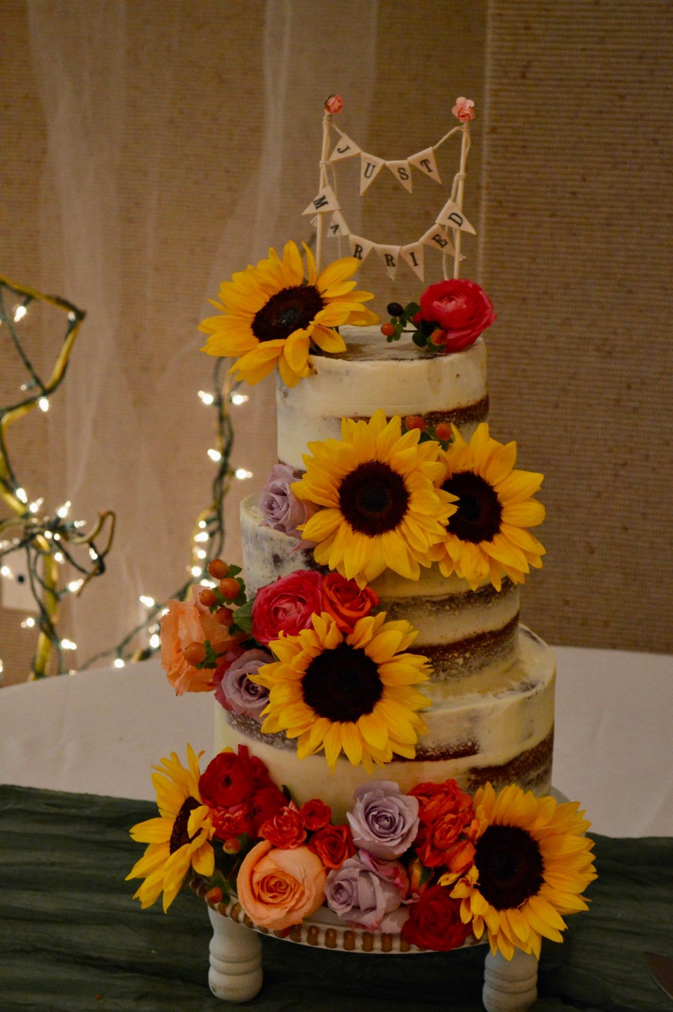 Three-tier semi-naked wedding cake topped with sunflowers and red roses